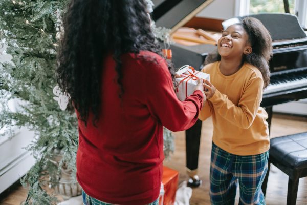 Crop ethnic mother giving Christmas present to happy girl